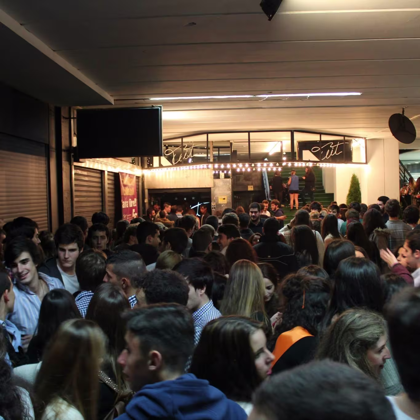 Discoteca Nuit: Punto de encuentro para jóvenes, con un ambiente lleno de energía y largas filas de personas esperando para entrar. La entrada iluminada con luces festivas.