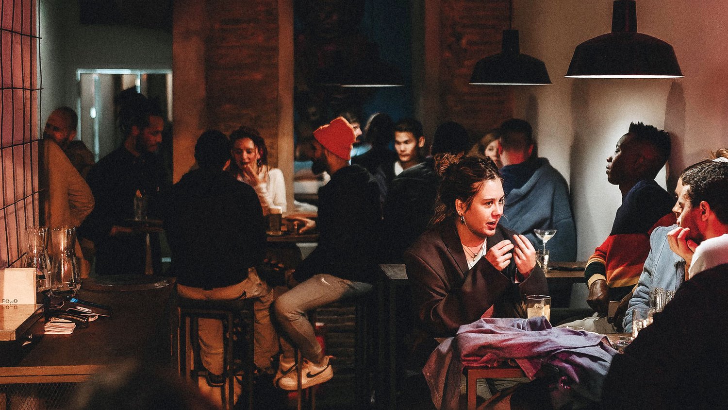 En Foco Bar, un ambiente animado reúne a grupos conversando bajo luces cálidas, con un estilo industrial y paredes de ladrillo expuesto.