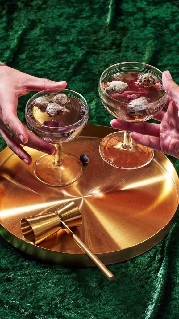 Un brindis elegante en Archy, copas de cóctel sofisticadas sobre una bandeja dorada, destacando un ambiente de lujo y estilo exclusivo.