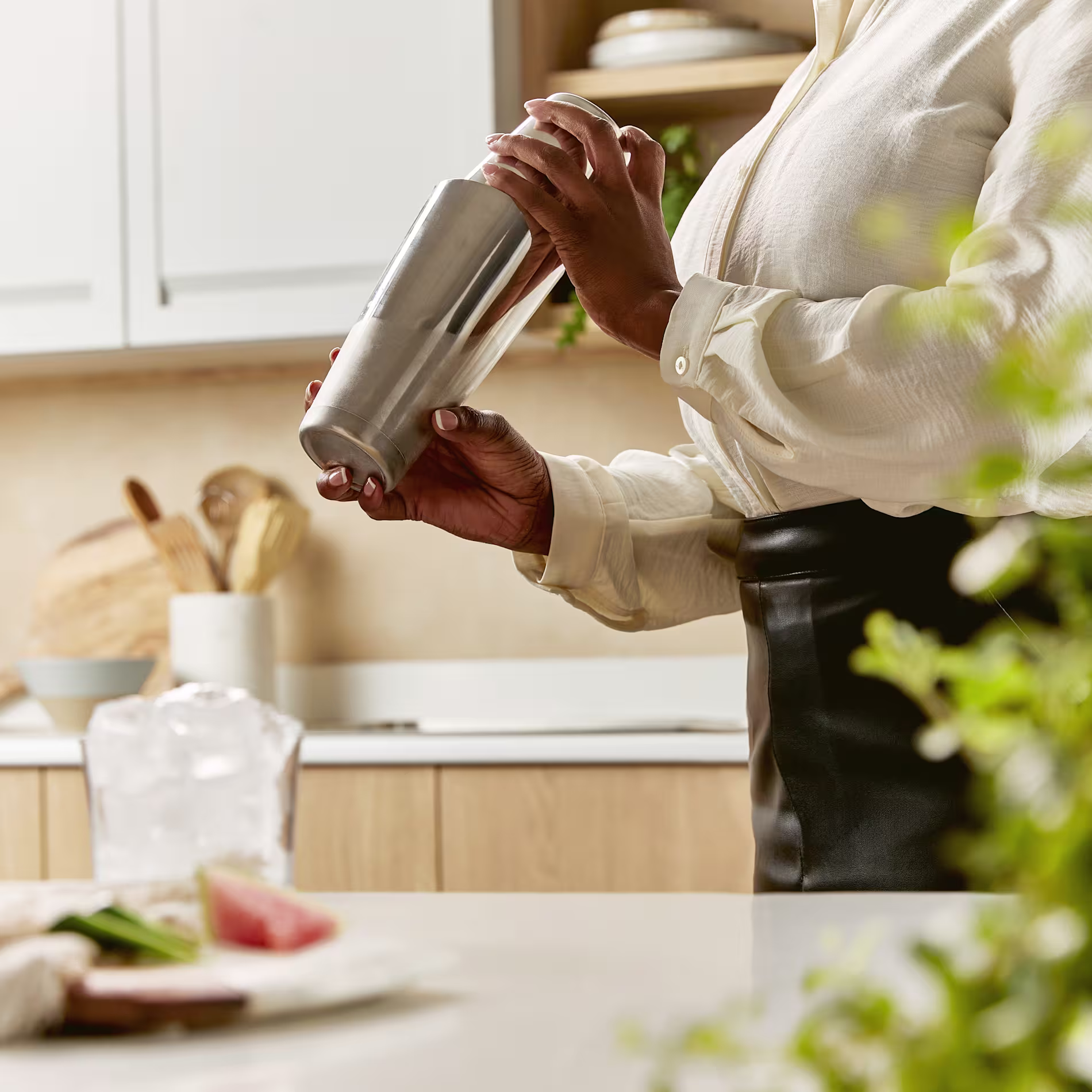 A bartender shakes a margarita in a silver cocktail shaker in a bright kitchen.