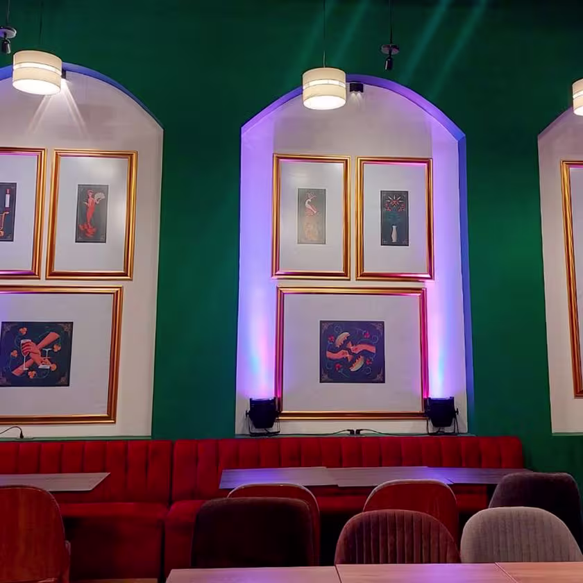 Imagen de las paredes decoradas con cuadros con marcos dorados. Sillones rojos  y meses.