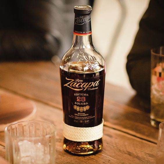 La imagen muestra una botella de ron Zacapa 23 y cuatro vasos dispuestos alrededor.