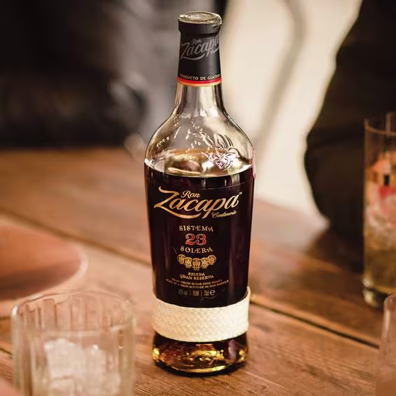 La imagen muestra una botella de ron Zacapa 23 y cuatro vasos dispuestos alrededor.
