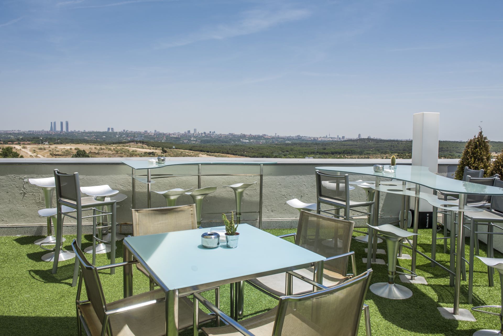 Terraza de El Cielo de Urrechu con mesas de cristal, sillas modernas y vistas panorámicas a Madrid en un ambiente soleado y relajado.