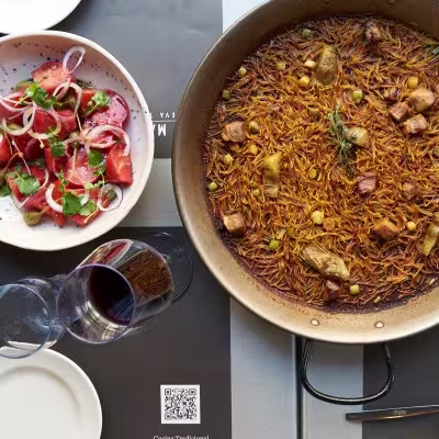 Fideuá dorada y ensalada de tomate con cebolla y aceitunas en Los Madriles Taberna, todo listo para compartir con una copa de vino.