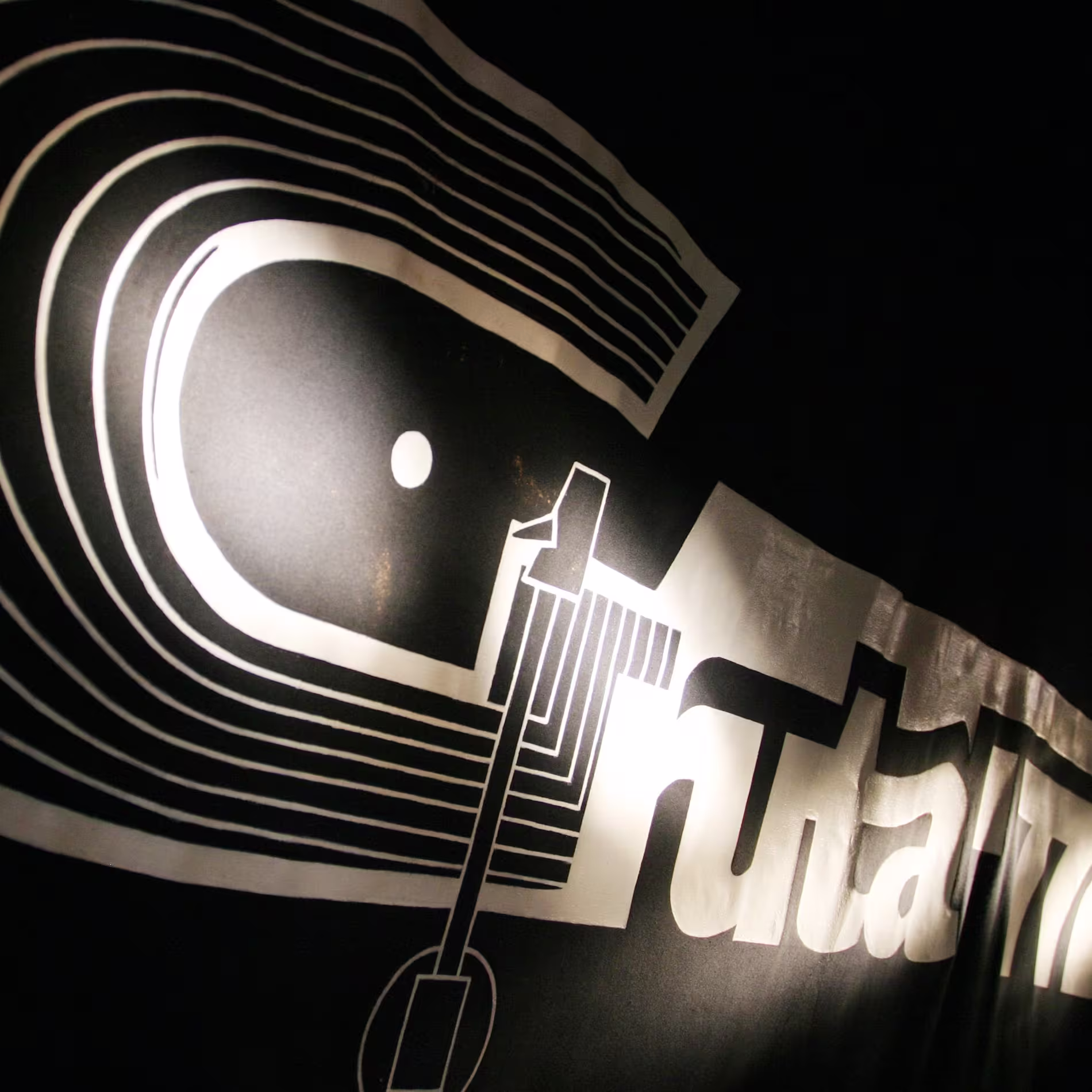 Logotipo en blanco y negro de Gruta 77, con diseño inspirado en vinilos y líneas curvas iluminadas sobre un fondo oscuro.