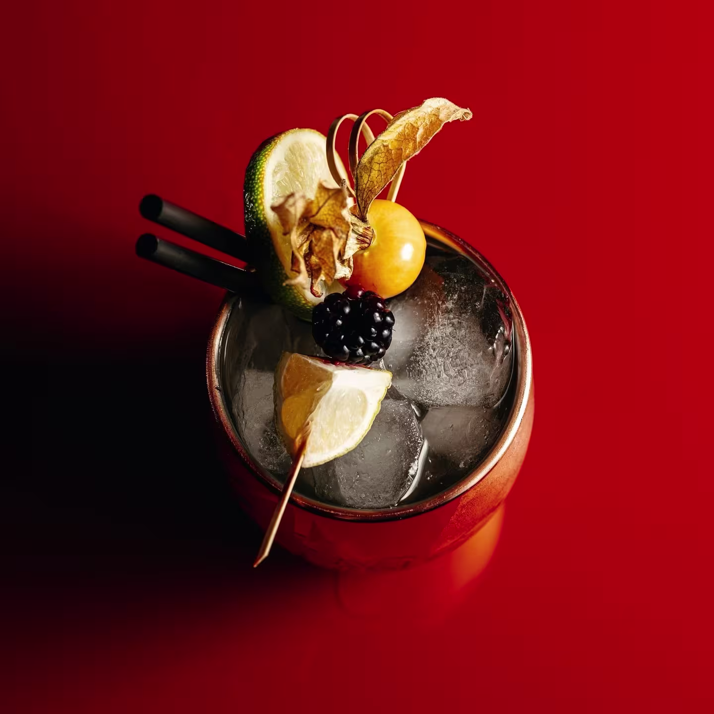 Cóctel de autor en Faena River Club, servido en vaso cobre sobre fondo rojo, con lima, mora, physalis y hielo. Elegancia vibrante.