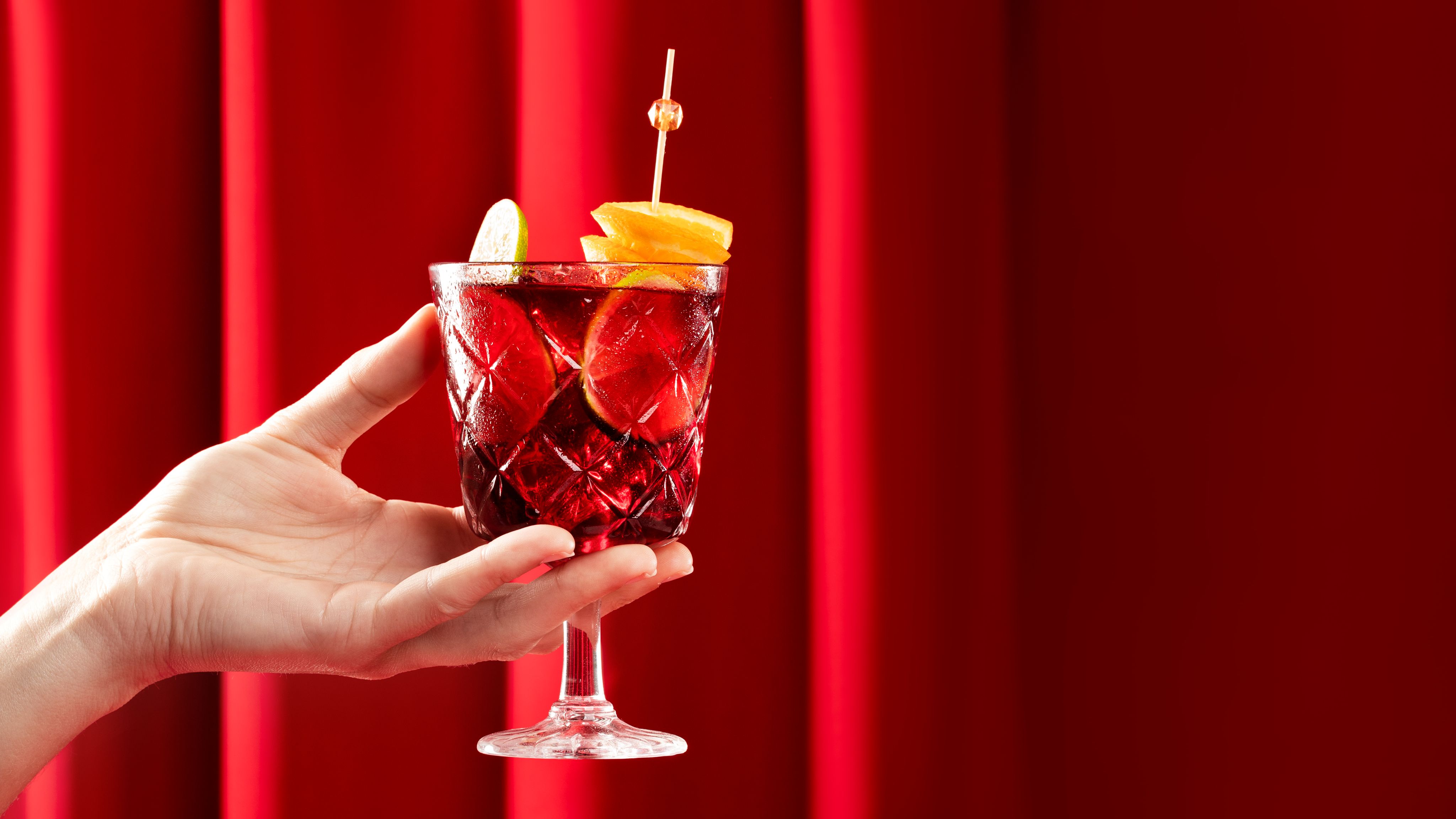 A glass of Sangria being held up against a red curtain backdrop