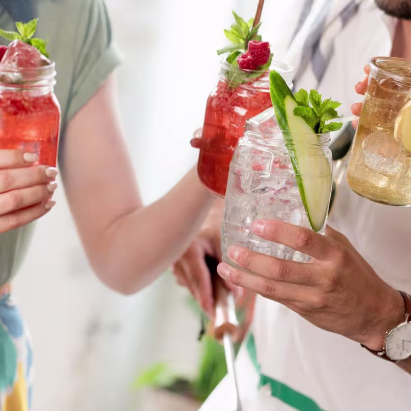 La imagen muestra cuatro copas con cócteles sostenidas por personas que aparecen de fondo.