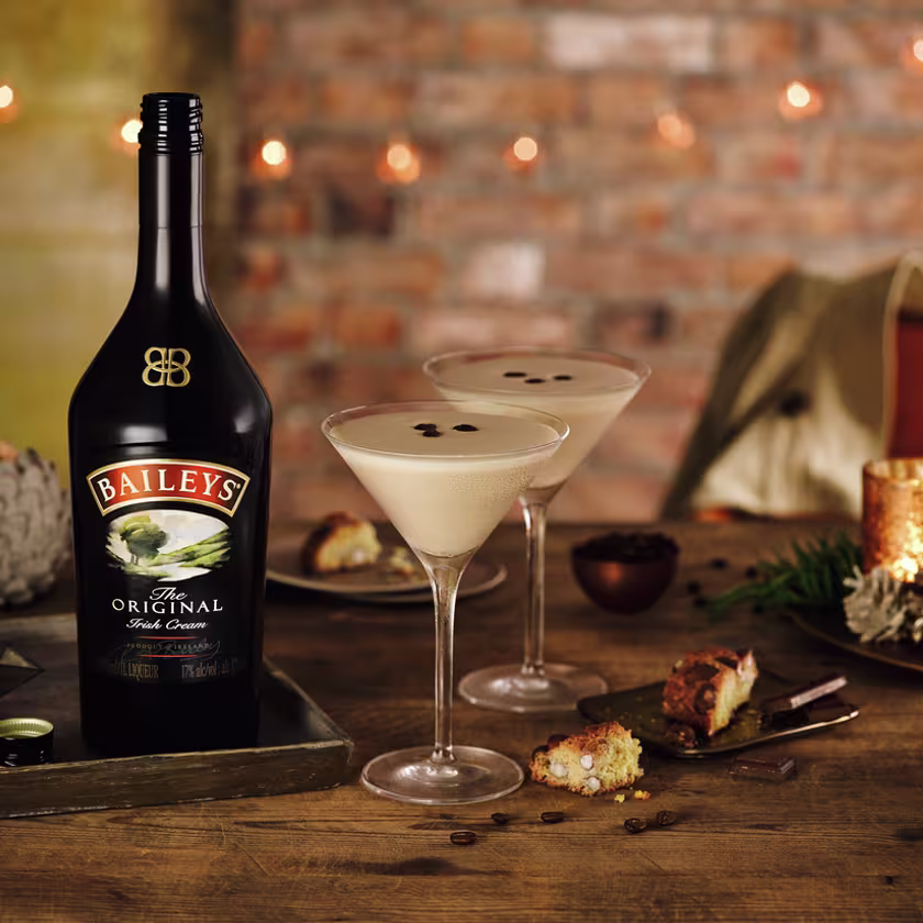 La imagen presenta una botella de Baileys Original Irish Cream junto a dos copas que contienen el cóctel Flat White martini.