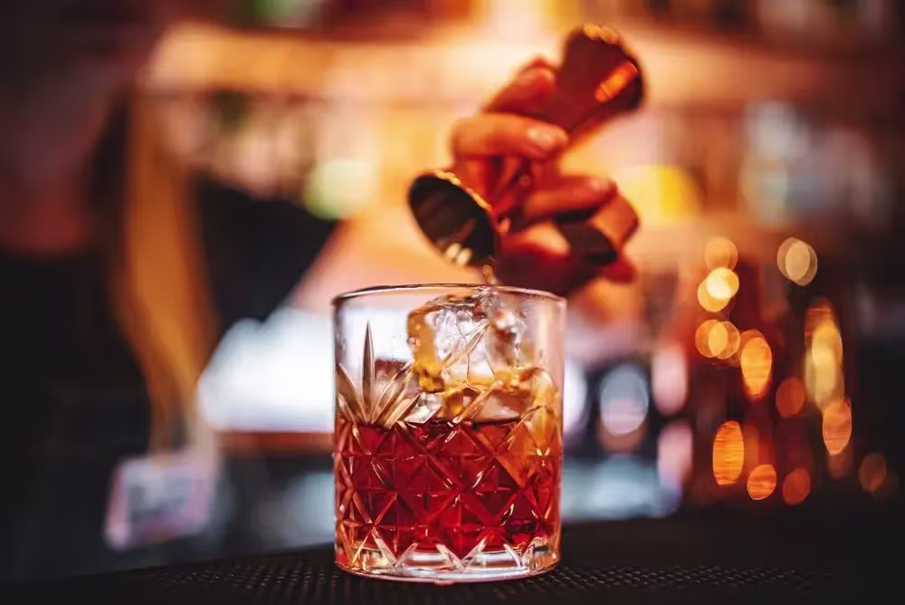 Bartender pouring a shot of Scotch into a glass with ice.