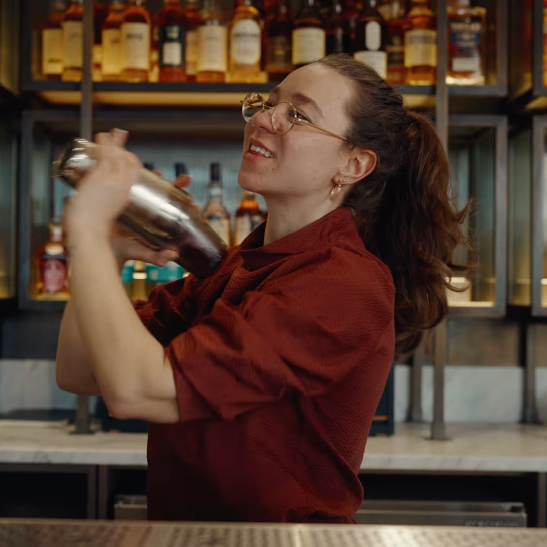 Charlotte Barker holding a cocktail shaker in front of a fully stocked bar.