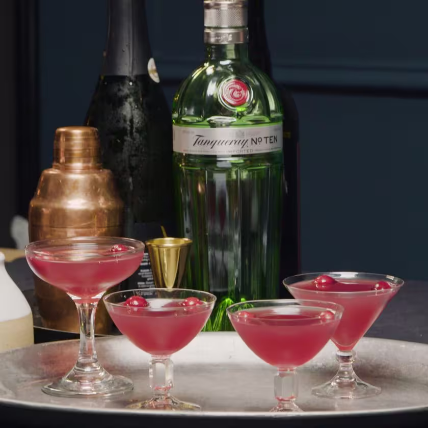 La imagen muestra una botella de gin Tanqueray n° TEN, elementos de coctelería y, por último, cuatro copas rellenas con cócteles preparados con dicho destilado sobre una bandeja de plata.