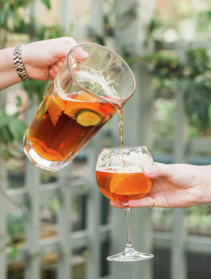 Egy kinyújtott kar egy korsó Pimmsből egy másik személy által tartott pohárba önti.