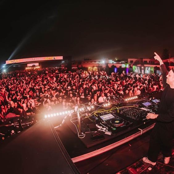 Multitud de gente bailando y el dj levantando la mano mientras toca