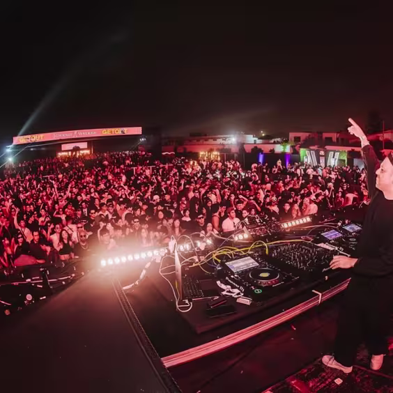 Multitud de gente bailando y el dj levantando la mano mientras toca
