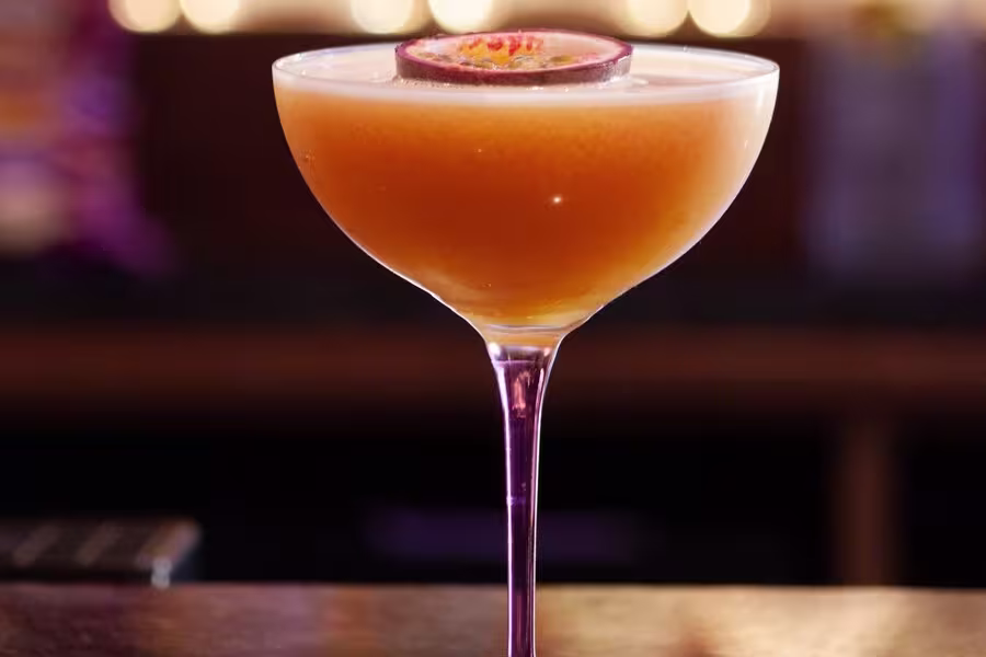 A cocktail in a coupe glass garnished with a halved passion fruit floats on top.