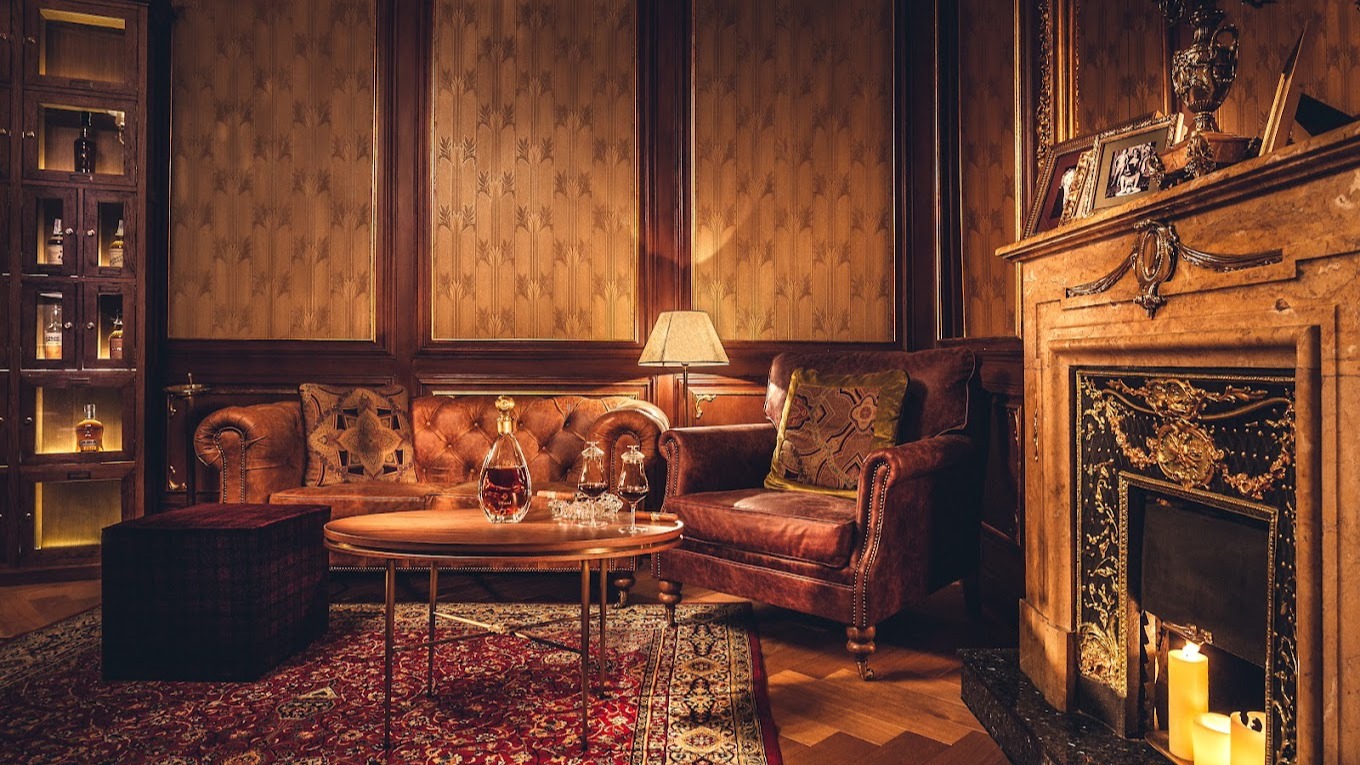 Salón elegante con sofás de cuero, alfombra persa, chimenea encendida y una mesa con decantador de licor y copas, ambientado con luz cálida.