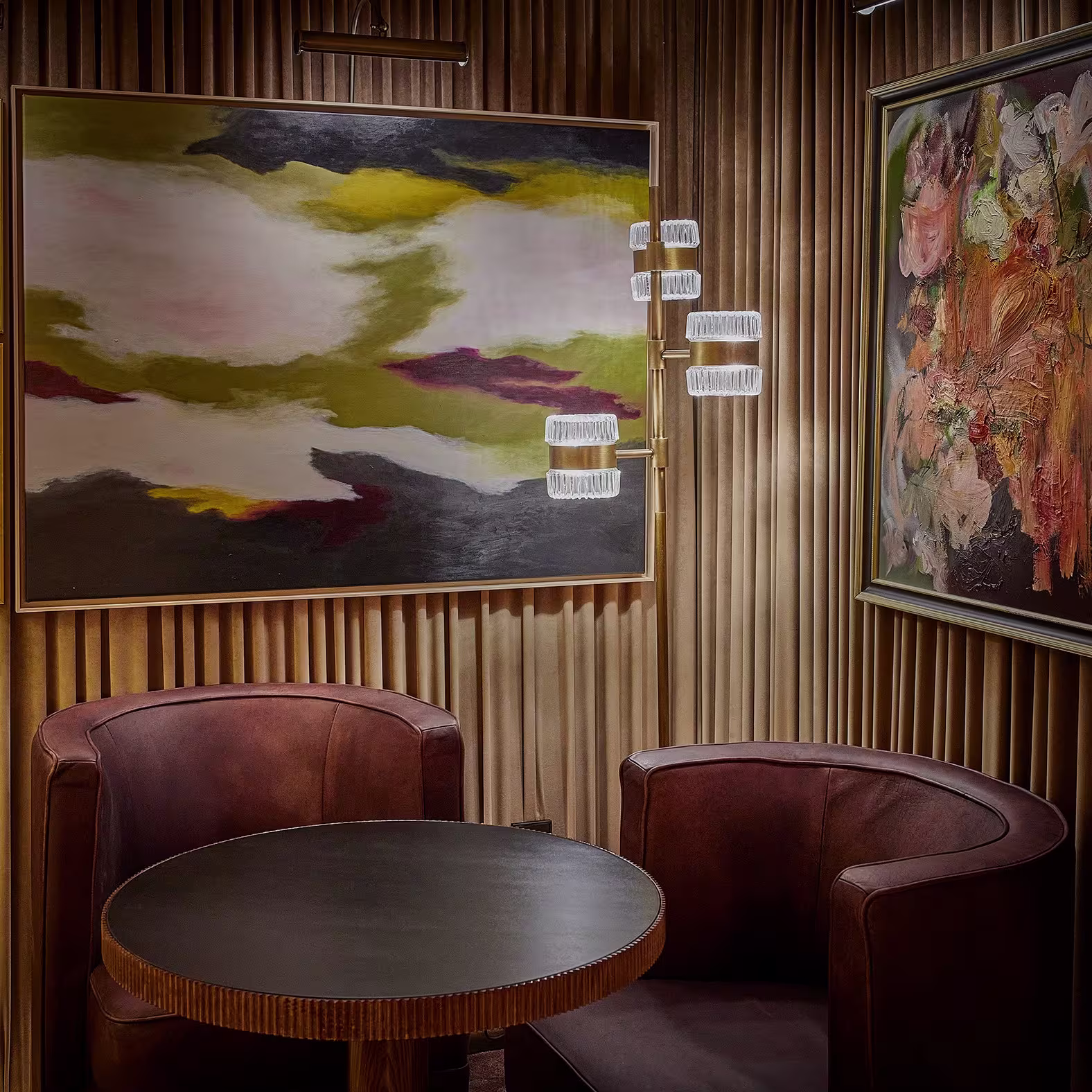  Espacio interior de el Coleccionista. En el centro, hay una mesa redonda de madera, flanqueada por dos sillones de felpa con tapicería marrón. 