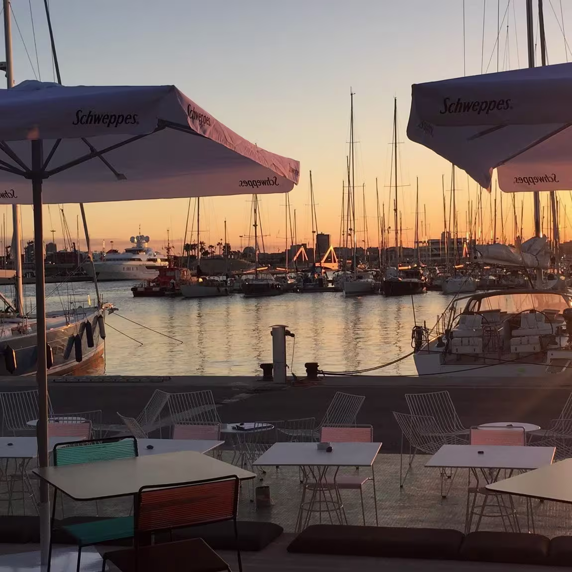 Terraza moderna con sillas de rayas, sombrillas redondas y mucha gente disfrutando del ambiente al atardecer frente a un local con cartel de "Azul".
