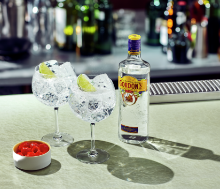Botella de gin Gordon´s, 2 copas de vidrio llenas de hielo, rodaja de limón en cada una como decoración y un pote con cerezas. Colocados en una barra