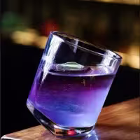 En la imagen se ve un cóctel con un vaso por particular, de forma inclinada, en color morado.