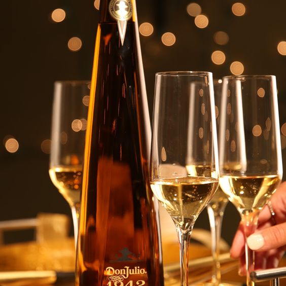 La imagen muestra una botella de Tequila Don Julio 1942 junto a tres copas llenas con dicho destilado.