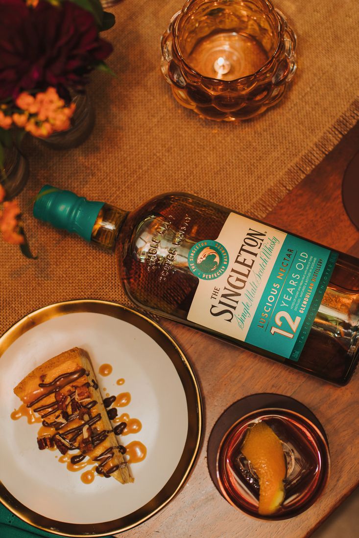 La imagen muestra una botella de whisky The Singleton 12 años junto a una porción de torta, y un vaso con el cóctel Old Fashioned.