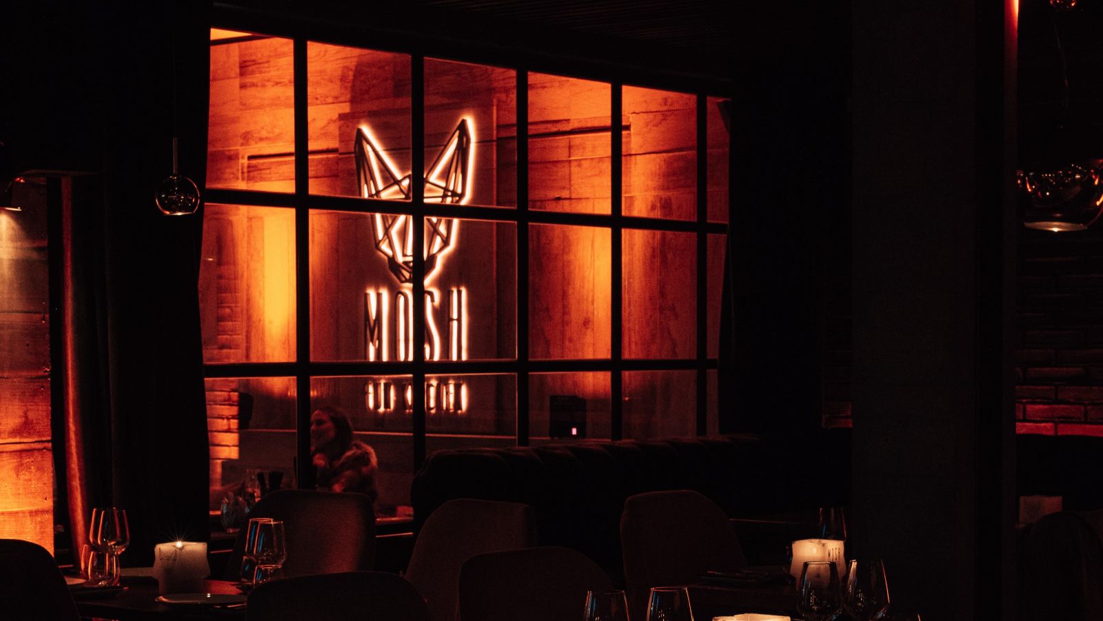 Mosh Fun Kitchen, elegante ambiente nocturno con iluminación cálida y el icónico logo, creando una atmósfera vibrante y acogedora.