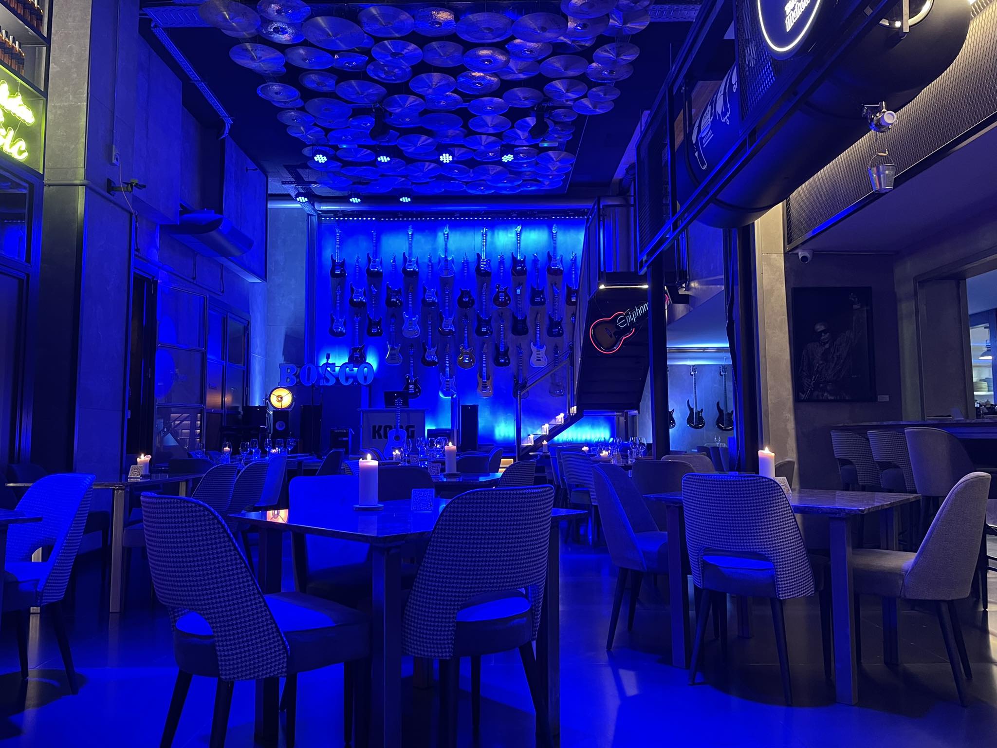 Interior de Bosco, con iluminación azul, decoración de guitarras en la pared y un ambiente vibrante ideal para cenas y música en vivo.