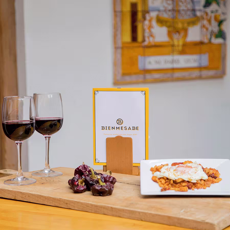 Una tabla en Bienmesabe Santa Engracia con dos copas de vino, un plato de migas con huevo frito y pimientos secos, rodeada de un ambiente andaluz.