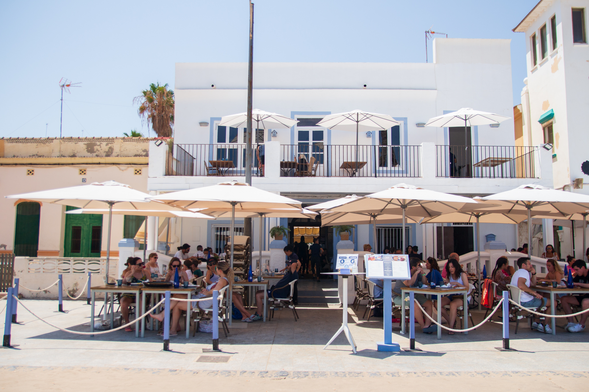 Terraza de Casa Patacona con mesas bajo sombrillas, ambiente relajado y fachada blanca frente al mar, ideal para disfrutar de un arroz junto a la playa.