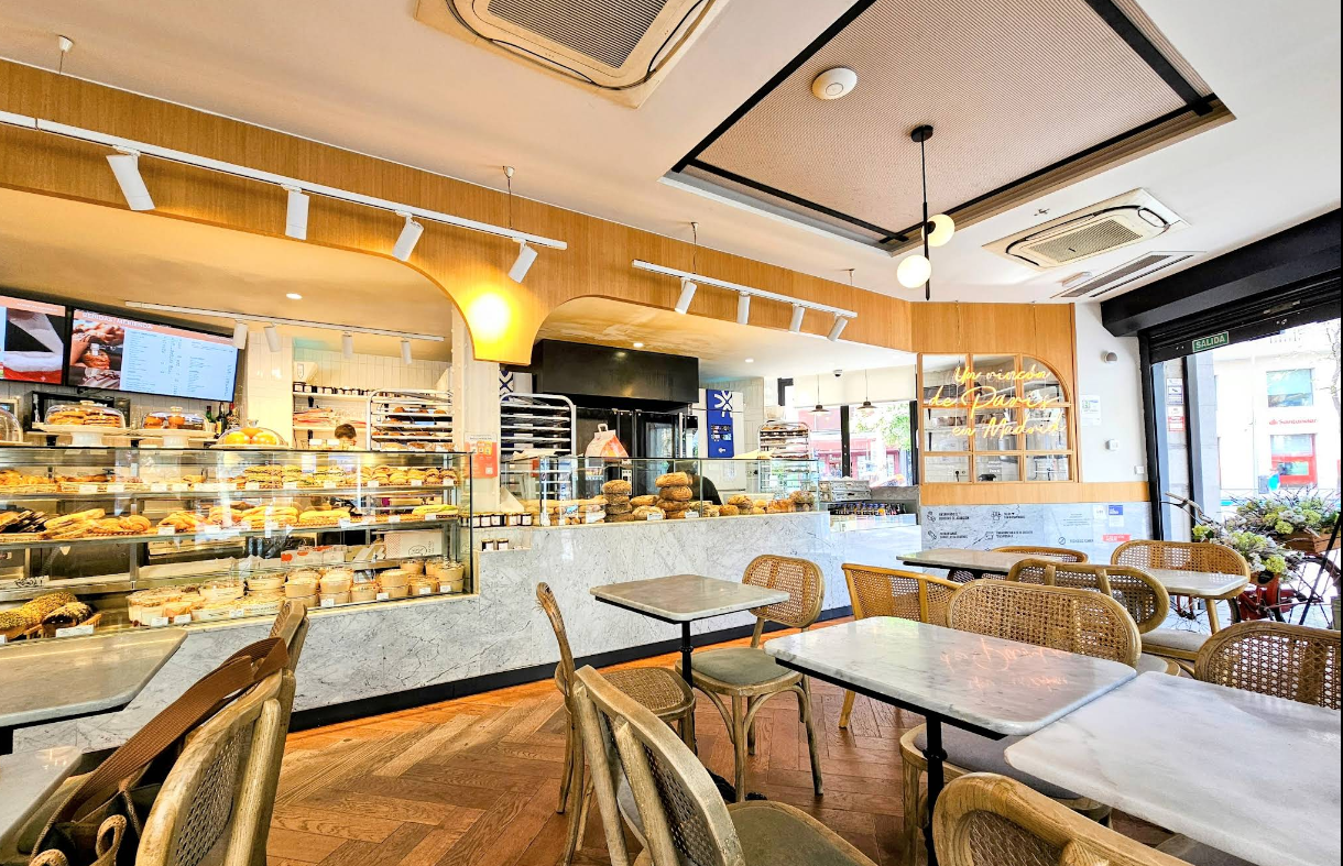 Interior de Maison Kayser en Príncipe de Vergara, con vitrinas llenas de pan y repostería artesanal, mobiliario de madera clara y un ambiente luminoso y moderno.