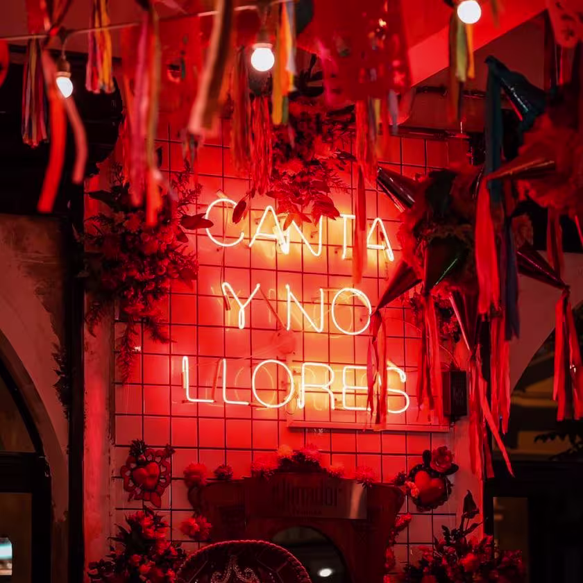 Imagen de cartel luminoso rojo, con la frase CANTA Y NO LLORES
