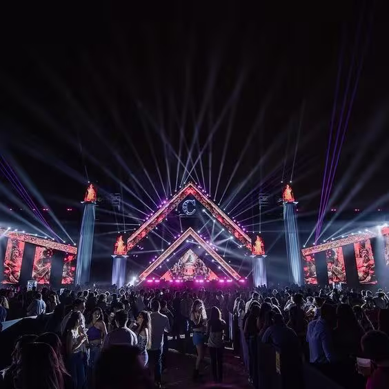 En la imagen se observa una vista panorámica de la fiesta Cochinola, con una gran concurrencia de personas. En el fondo, destaca un imponente escenario que recrea un castillo y está iluminado con numerosas luces.