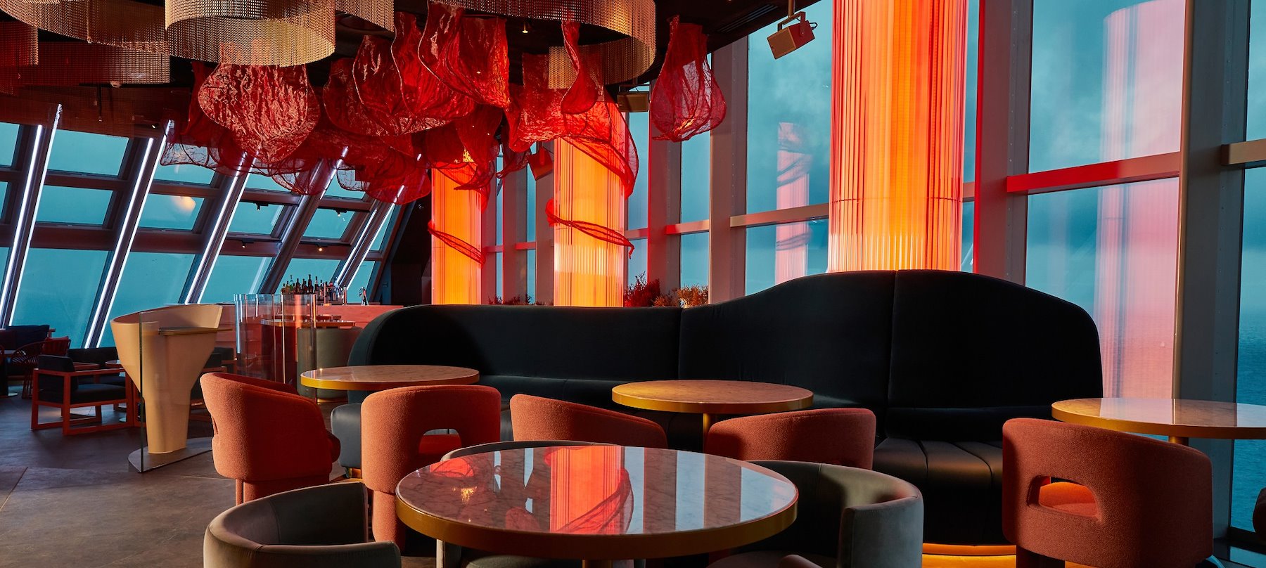 Noxe Barcelona, un espacio moderno con iluminación roja envolvente, mesas elegantes y vistas panorámicas desde su ubicación elevada.