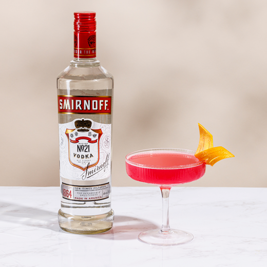 Copa de Cosmopolitan con un gajo de naranja en el borde, junto a una botella de Smirnoff N°21