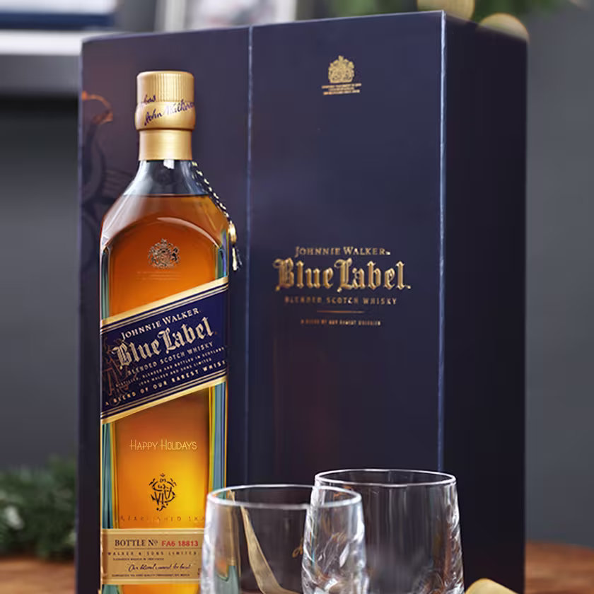 En la imagen se observa una botella de whisky Blue Label junto a su caja de empaque y dos vasos de whisky vacíos.