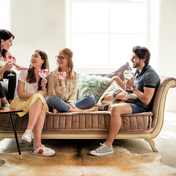 La imagen muestra a cuatro personas sentadas en un sillón, cada una con un cóctel en la mano.