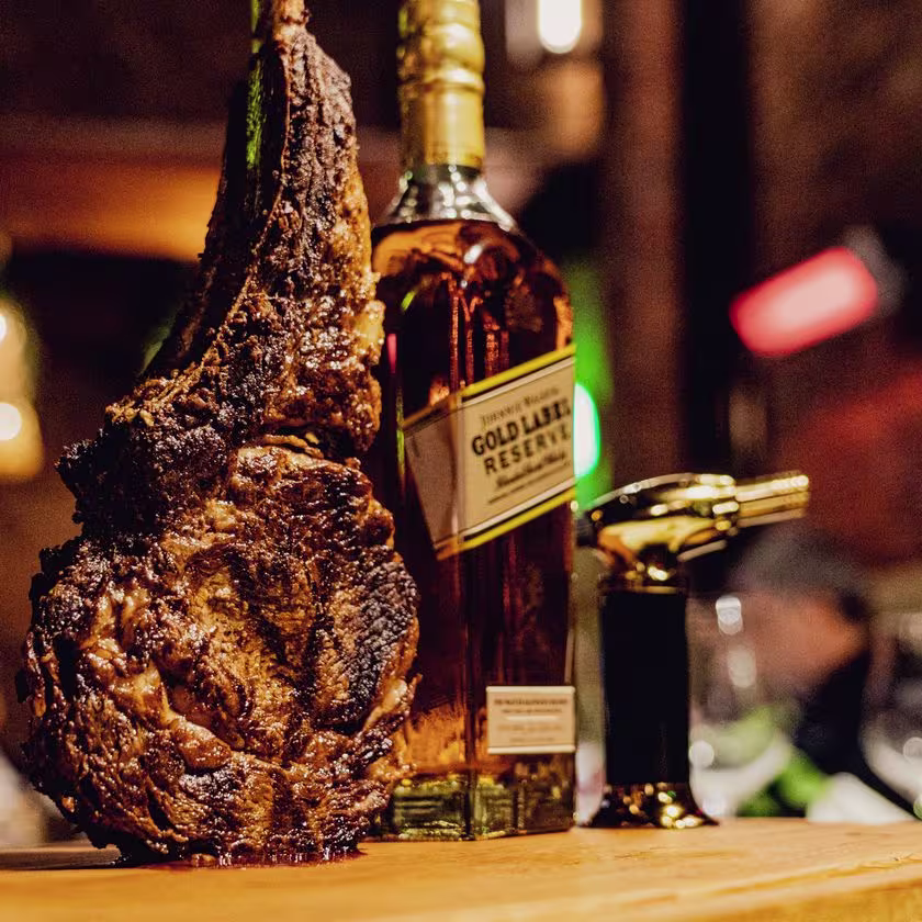 La estrella de la casa: el Tomahawk Gold está suspendido sobre la tabla donde lo flamean. A su lado, una botella de Johnnie Walker Gold y el mechero dorado que usan para esta experiencia única.