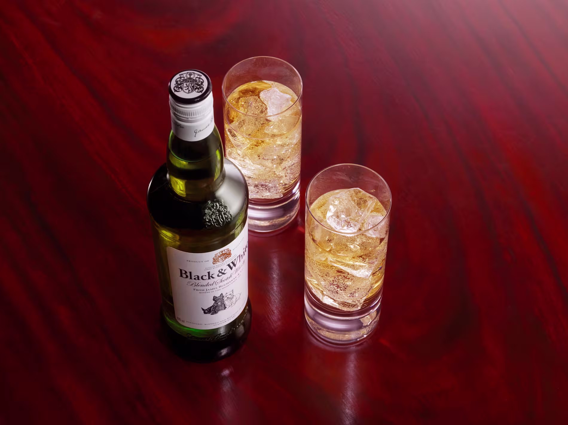 Black & White whisky bottle with two glasses of whisky and ice on a polished wooden table