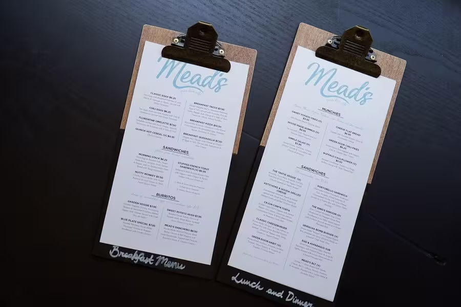 Two clipboards display Meads restaurant menus; the left is labeled Breakfast Menu and the right Lunch and Dinner Menu, both printed with multiple food options on white paper.