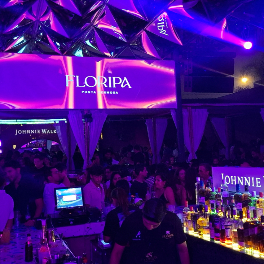 En la imagen se ve el contexto de la disco Floripa. La luz es violeta, hay una pantalla rectangular alta en la pista, y se ve la barra en el centro.