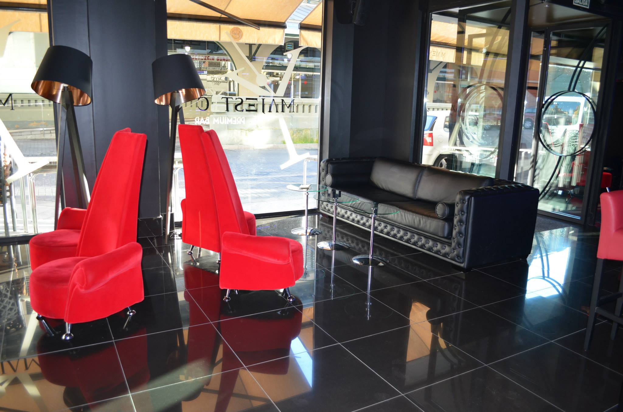 Majestic Premium Bar con elegantes sillas rojas y sofás negros, un ambiente moderno y sofisticado con decoración minimalista y acabados brillantes.