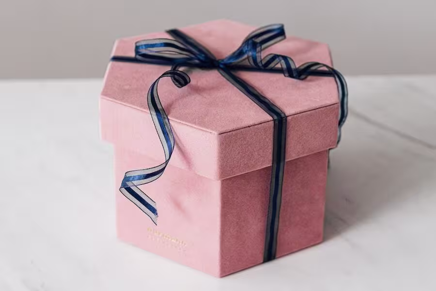 A pink, hexagonal gift box with a dark blue ribbon tied in a bow sits on a white surface.