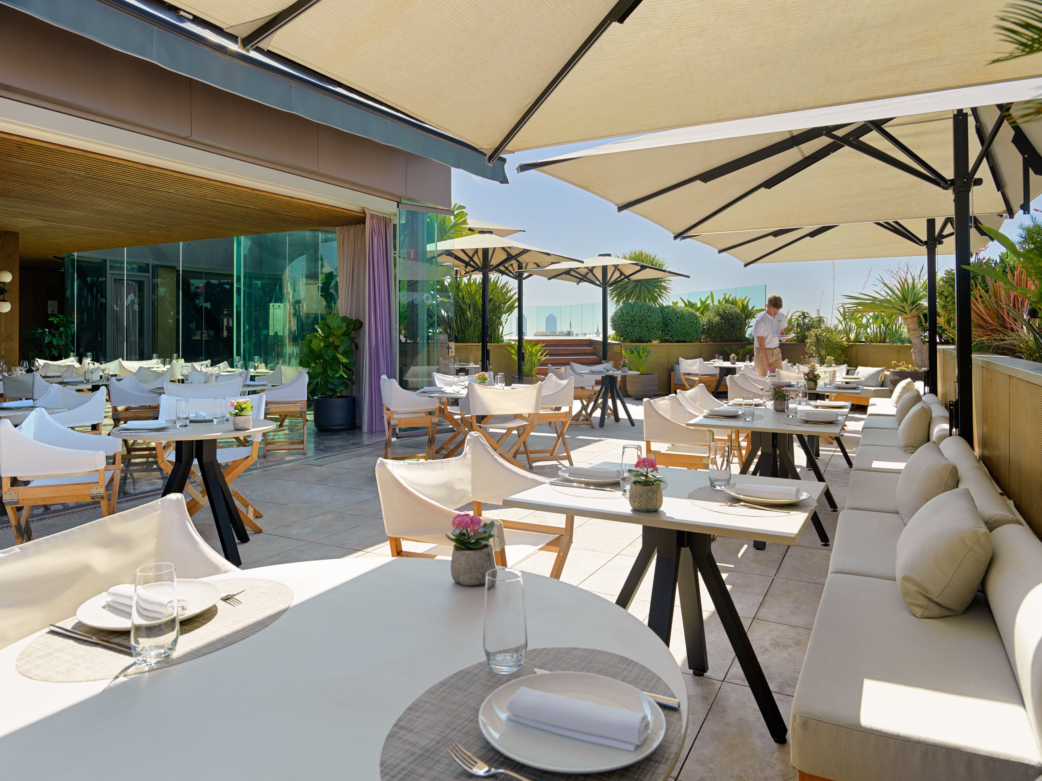 Terraza de Mood Rooftop Bar con mesas elegantes, cómodos asientos y sombrillas, rodeada de vegetación y vistas panorámicas al horizonte.