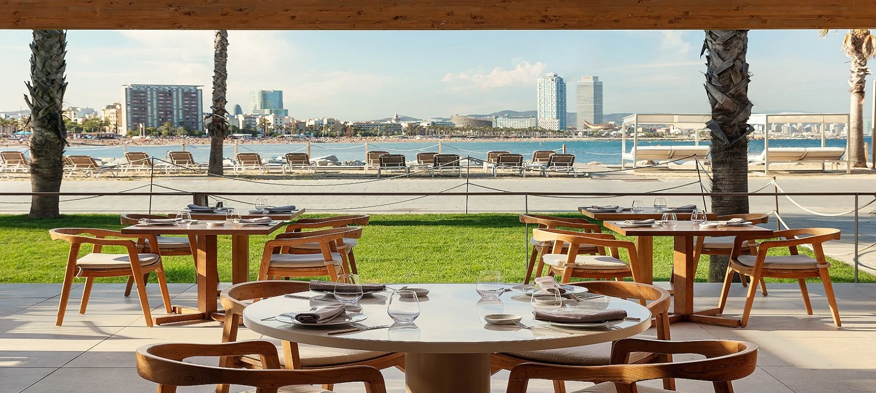 Vista desde SALT Restaurant & Beach Club, con mesas al aire libre frente al mar, césped y la playa de Barcelona como fondo.