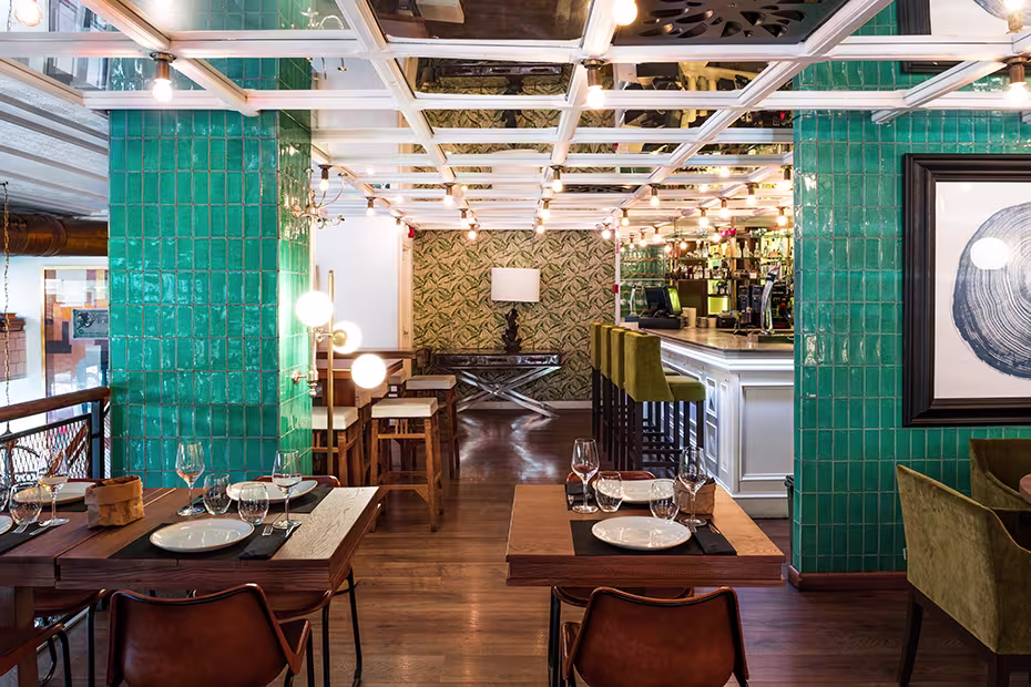 Elegancia y frescura en Casa Mono con su decoración vibrante de azulejos verdes, mesas listas para recibir y una barra acogedora al fondo.