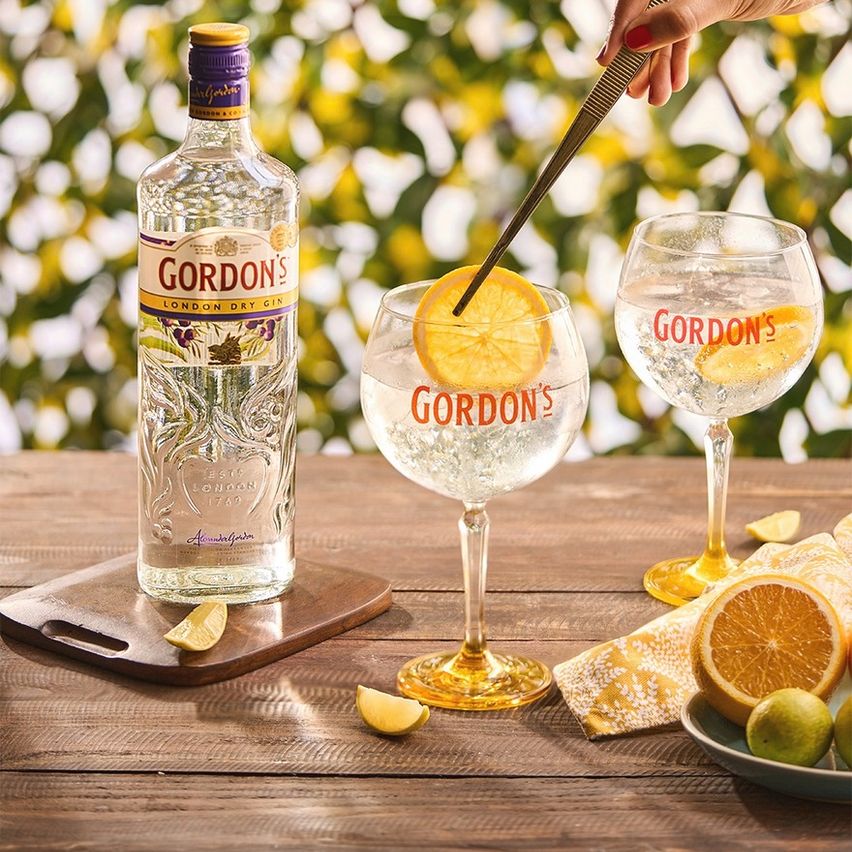 La imagen muestra una botella de gin Gordon's, dos cócteles preparados con dicho destilado y otros elementos de coctelería