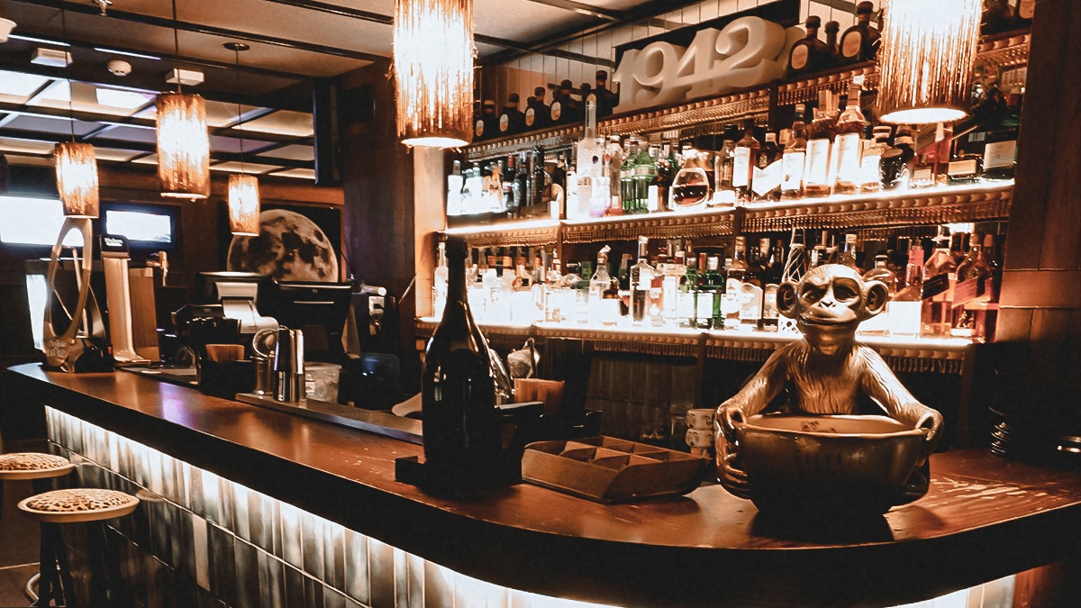 Fetén by Salvaje Barra moderna con iluminación cálida, estanterías llenas de botellas y detalles únicos como un mono decorativo.